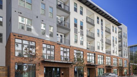 Photo of a new mid-height apartment complex with an eclectic exterior that includes a brick facade and large, industrial-style windows on the first two floors.