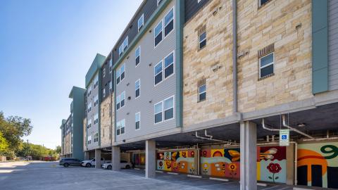 Photo of a contemporary four-story apartment complex with covered parking and murals on the ground floor.
